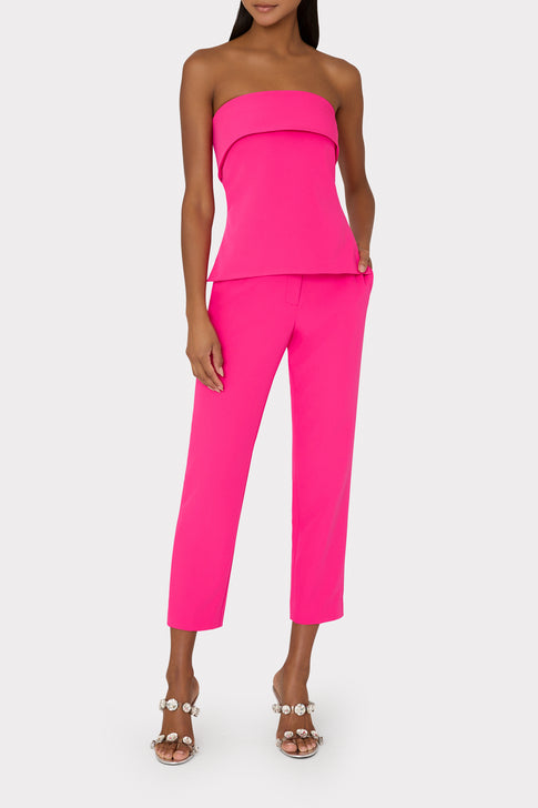 Woman wearing a bright pink strapless top and pants on a white background