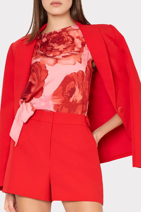 Person wearing a red blazer, pink floral top, and red shorts on a white background
