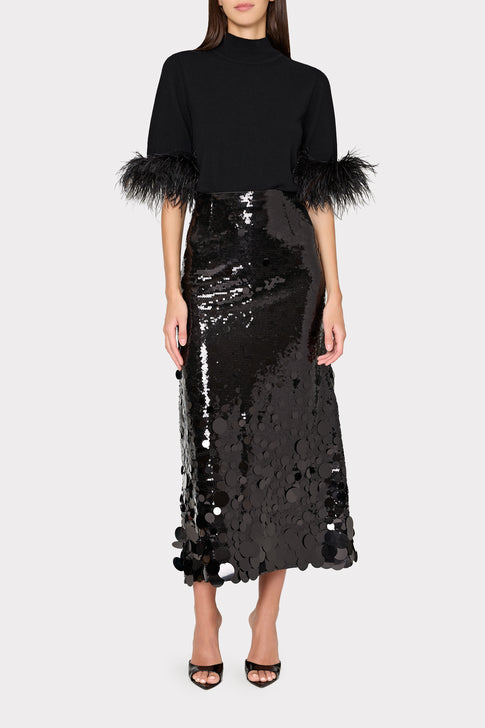 Woman wearing a black top with feathered sleeves and a black sequin skirt on a white background