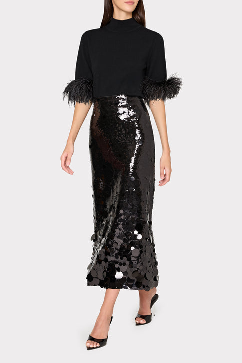 Woman wearing a black top with feathered sleeves and a black sequin skirt on a white background